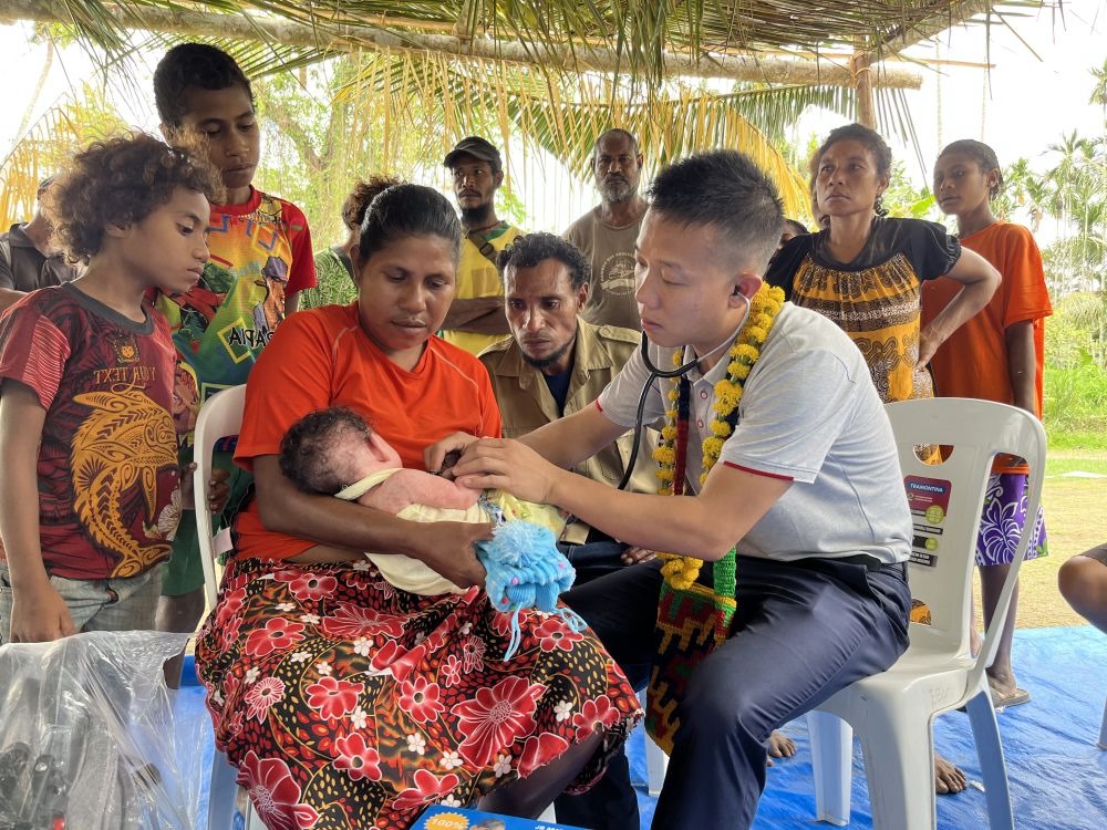 2023年8月5日，在巴布亞新幾內(nèi)亞中央省的一個(gè)村莊里，第12批援巴新中國醫(yī)療隊(duì)副隊(duì)長、新生兒科副主任醫(yī)師劉振球?yàn)閶雰禾仿犜\檢查。泰樂出生時(shí)患有重癥，一度生命垂危，經(jīng)過劉振球與當(dāng)?shù)蒯t(yī)護(hù)人員的救治最終痊愈。從2002年起，中國連續(xù)向巴新派出12批醫(yī)療隊(duì)，為提高巴新醫(yī)療衛(wèi)生水平作出積極貢獻(xiàn)。