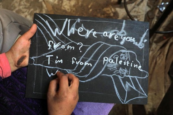 2023年12月28日，一名學(xué)生在加沙地帶南部城市拉法一所學(xué)校的臨時教室中寫下“我來自巴勒斯坦”的字樣。新華社發(fā)（里澤克·阿卜杜勒賈瓦德攝）